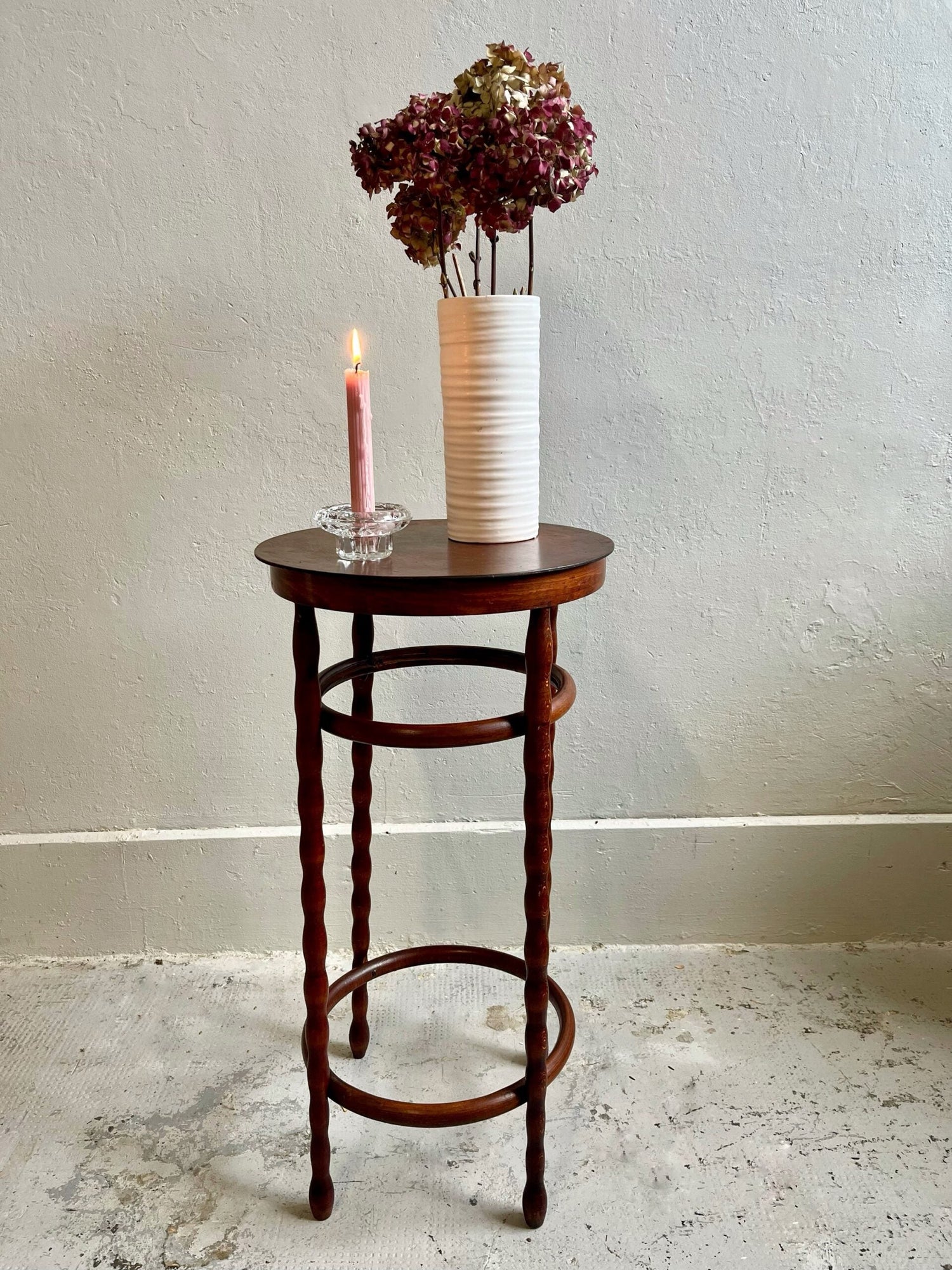 Guéridon ou sellette ou porte plante en bois foncé. Pieds tournés. Bouquet d'hortensia séchés, une bougie rose dans un bougeoir en verre
