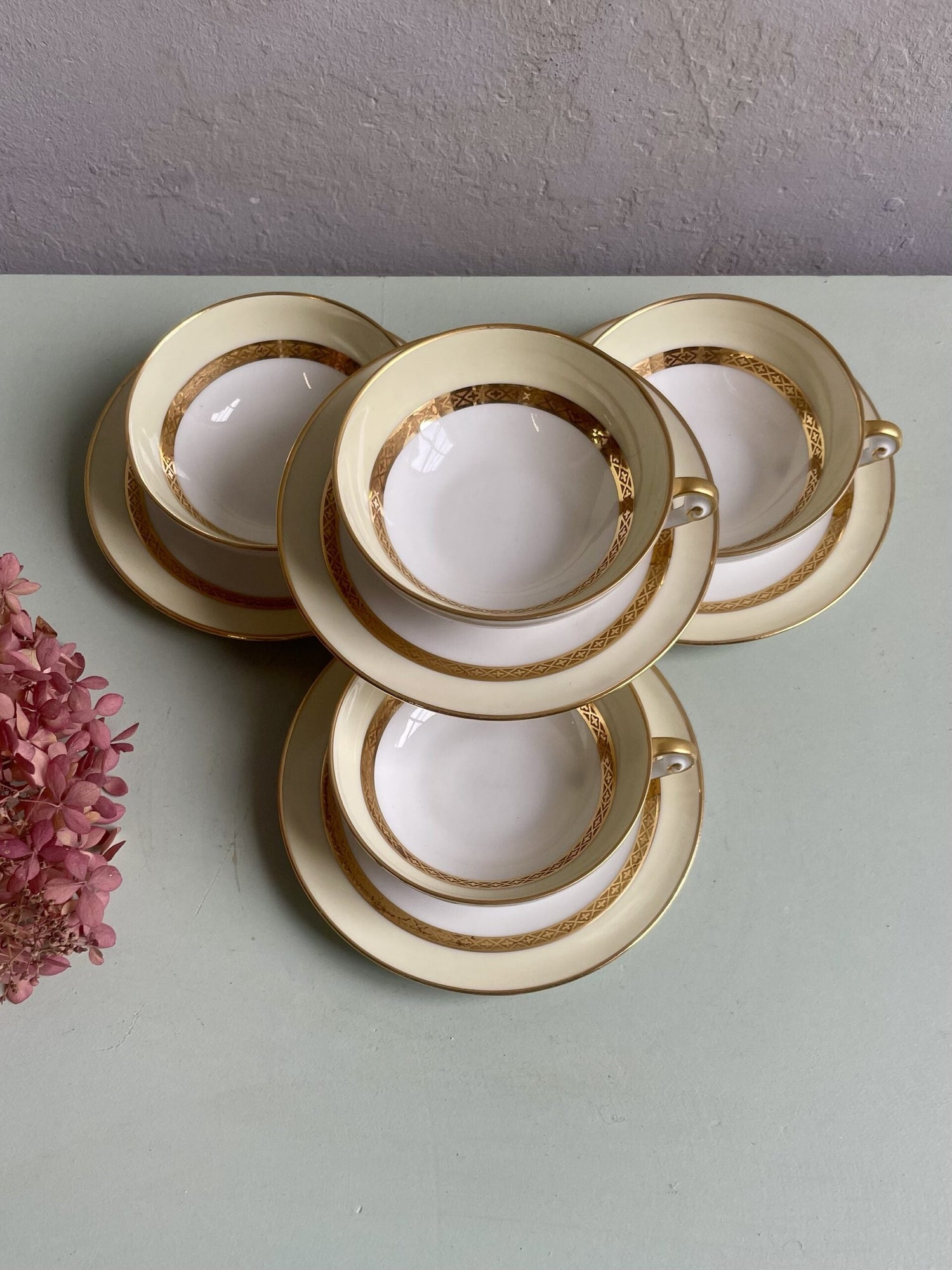 Vue du dessus de 4 tasses à thé et leur coupelle. Porcelaine fine jaune pale et blanche, relevé de doré travaillé avec un motif. 